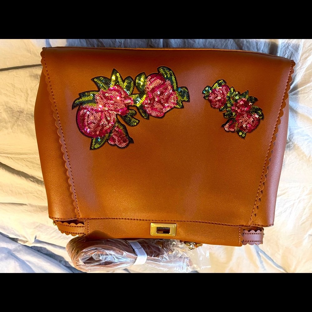 Tan purse with flower embroidery and shoulder strap.